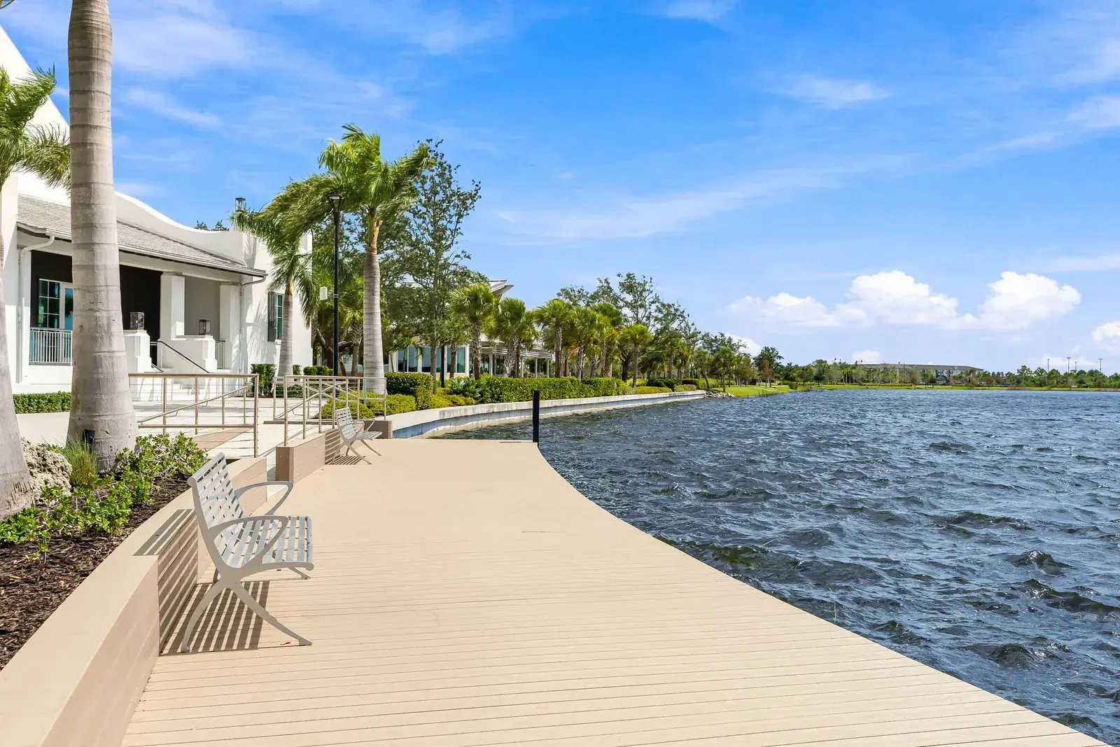 Wide lakefront boardwalk with benches and palms curving along the water in Wellen Park